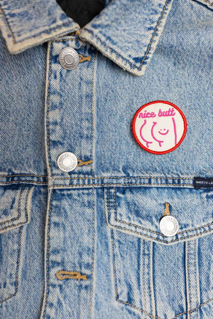 Patch brodat cu mesajul amuzant „Nice Butt” și față zâmbitoare, un accesoriu ironic și jucăuș pentru personalizare.