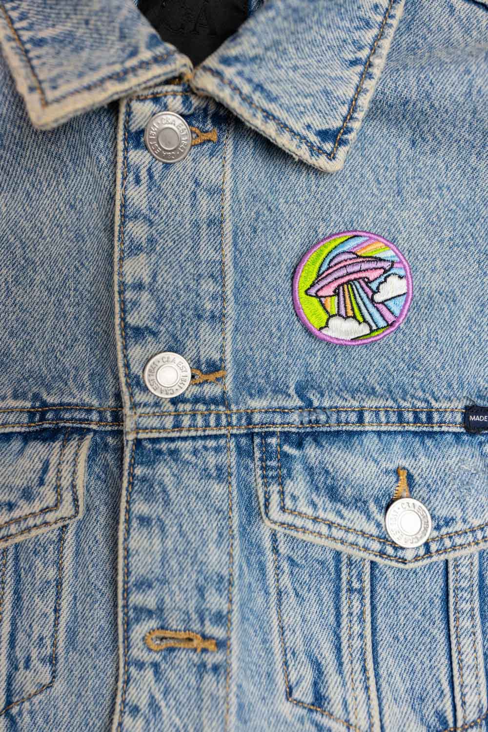 Patch brodat cu design colorat inspirat de un OZN pe fundal negru, un accesoriu creativ pentru iubitorii de modele neobișnuite.