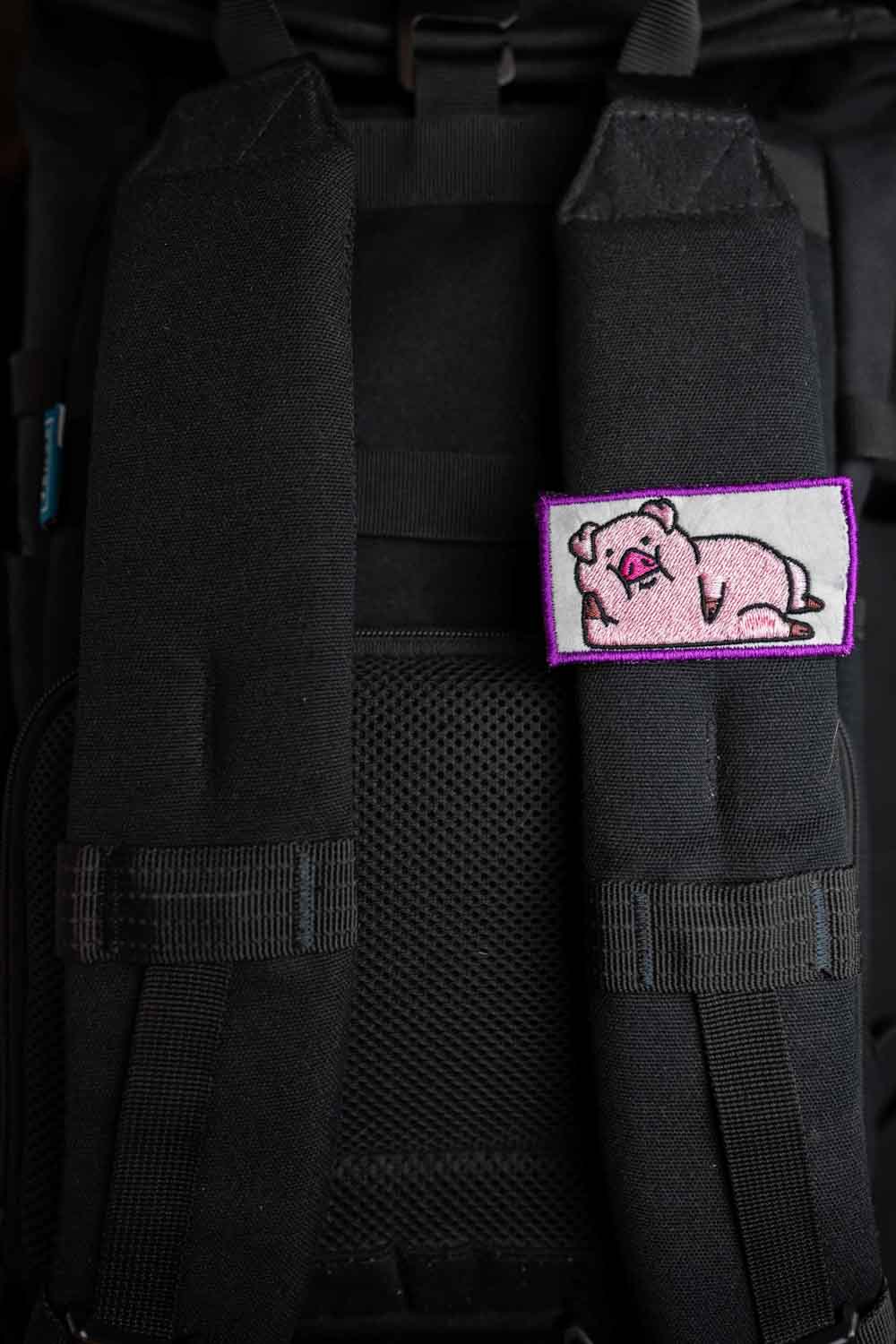 Patch brodat cu purcel roz pe fundal alb și margine mov, un accesoriu simpatic și colorat.
