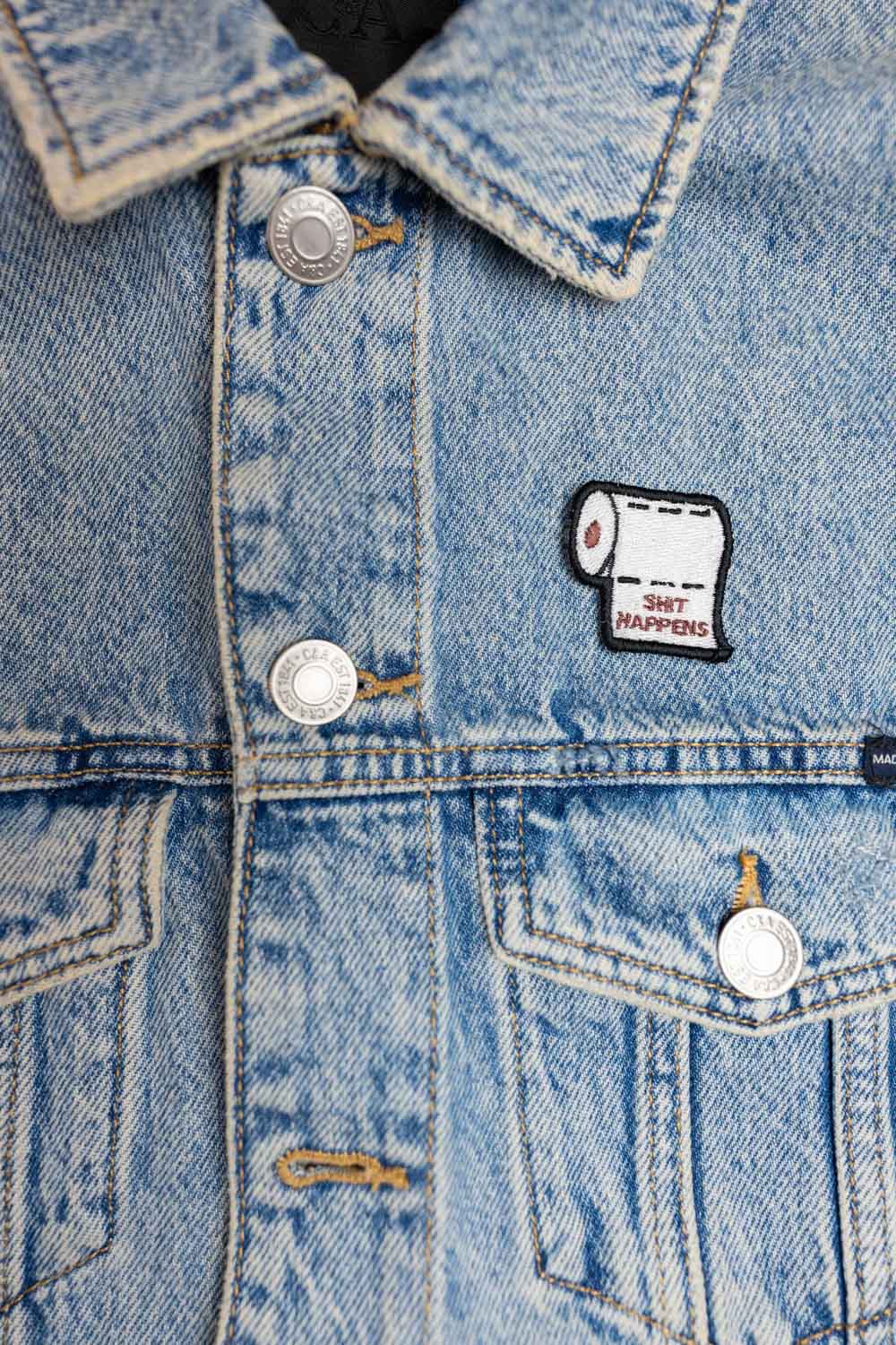 Patch brodat alb cu sul de hârtie igienică și mesajul „Shit Happens”, un design amuzant și ironic pentru haine sau accesorii.
