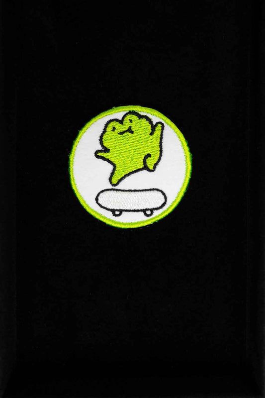 Patch brodat cu personaj stilizat pe skateboard, în culori verde și alb pe fundal negru, un accesoriu pentru iubitorii de skate.