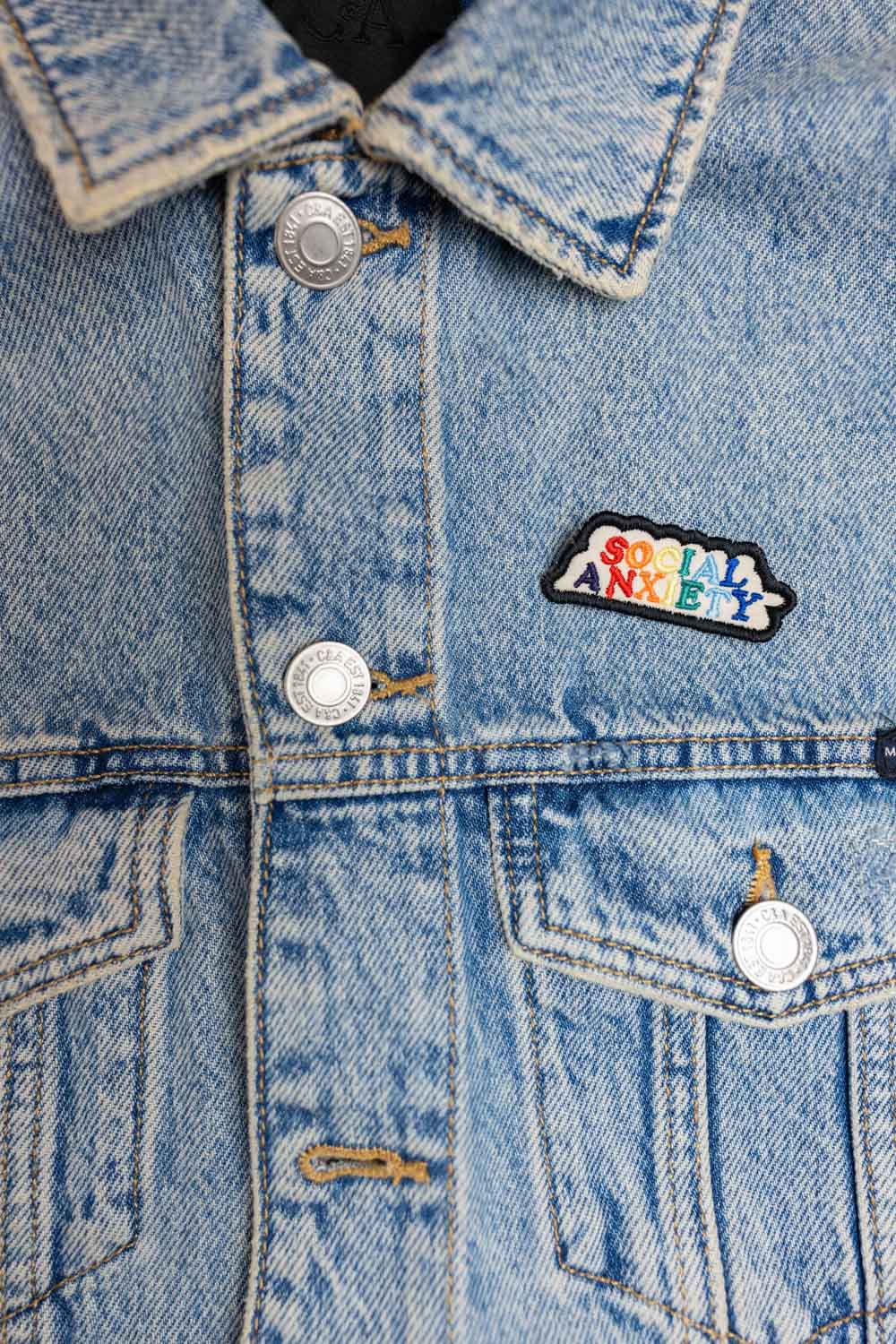 Patch brodat negru cu mesajul „Social Anxiety”, un accesoriu expresiv și ironic pentru personalizarea hainelor sau genților.