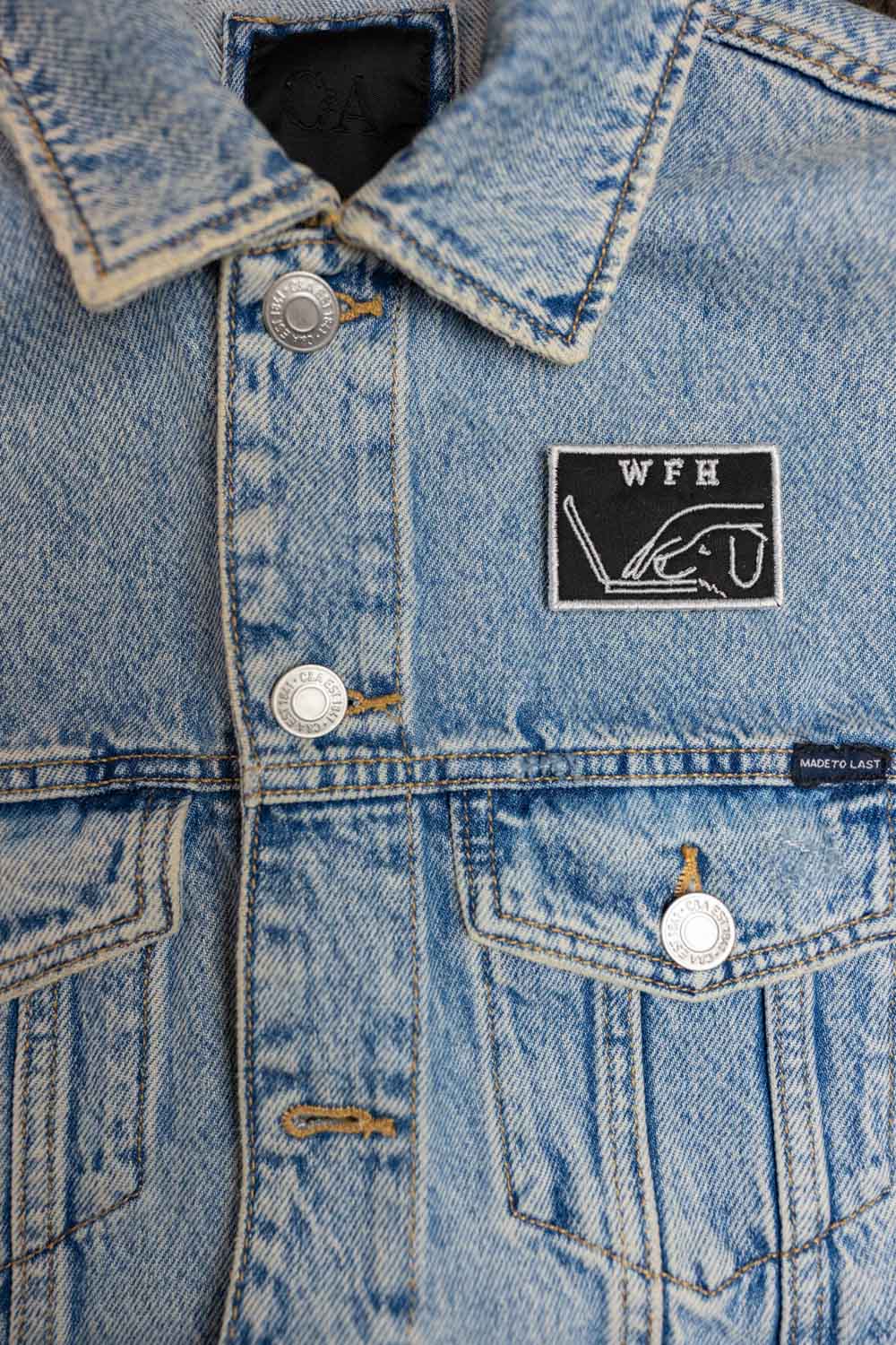 Patch brodat negru cu mesajul „WFH” și ilustrație de persoană cu laptop, un accesoriu pentru iubitorii muncii de acasă.