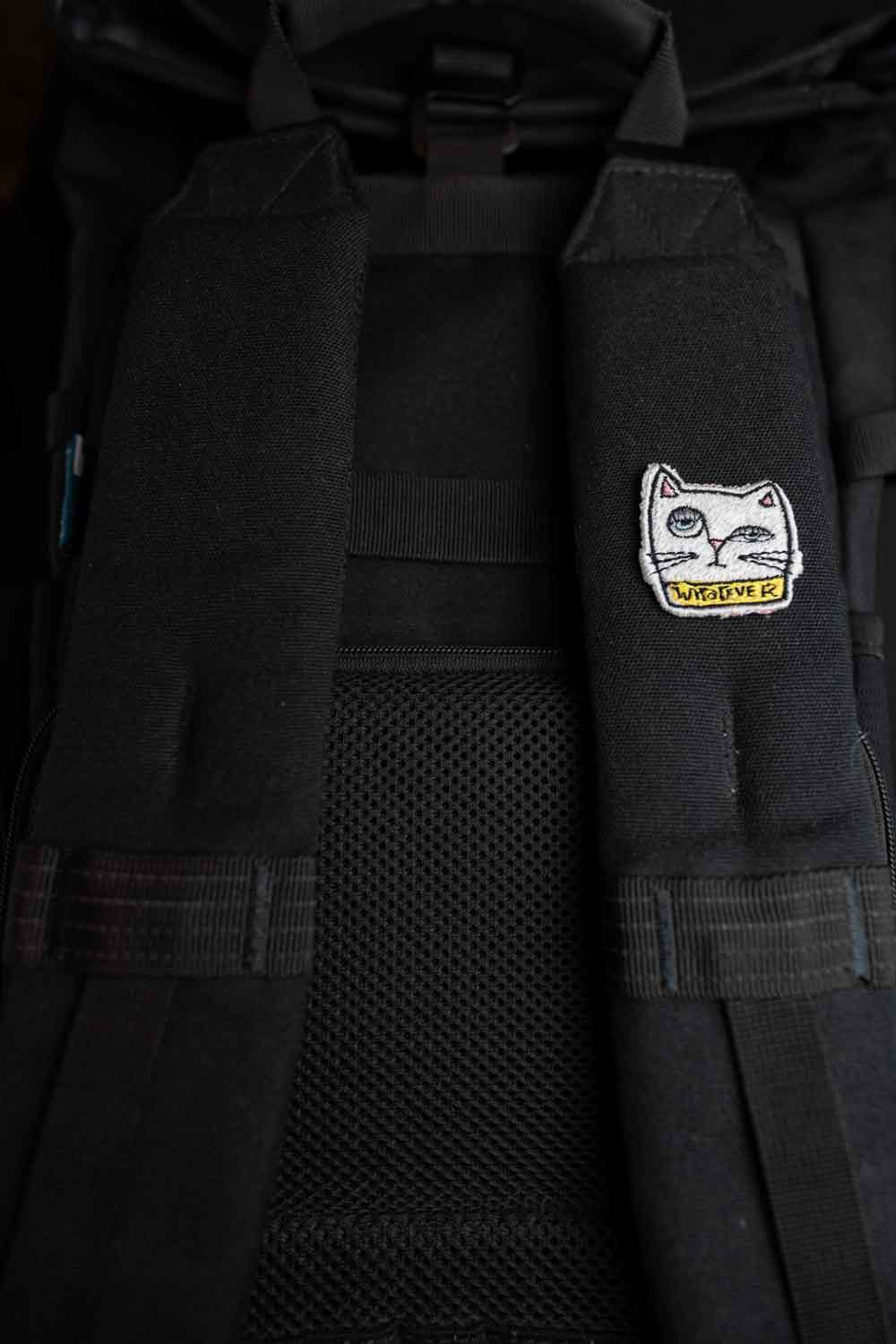 Patch brodat negru cu față de pisică albă și mesajul „Whatever”, un accesoriu ironic și amuzant pentru haine și genți.