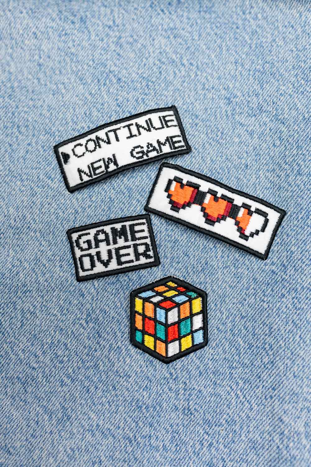 Set de trei patch-uri brodate cu tematică gaming, incluzând modelele „Continue New Game”, „Game Over” și Rubik Cube, prezentate pe material din denim.