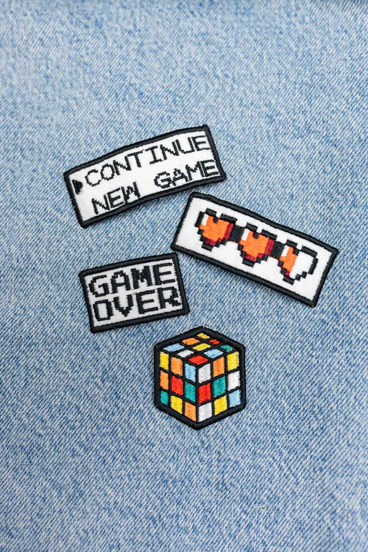 Set de trei patch-uri brodate cu tematică gaming, incluzând modelele „Continue New Game”, „Game Over” și Rubik Cube, prezentate pe material din denim.