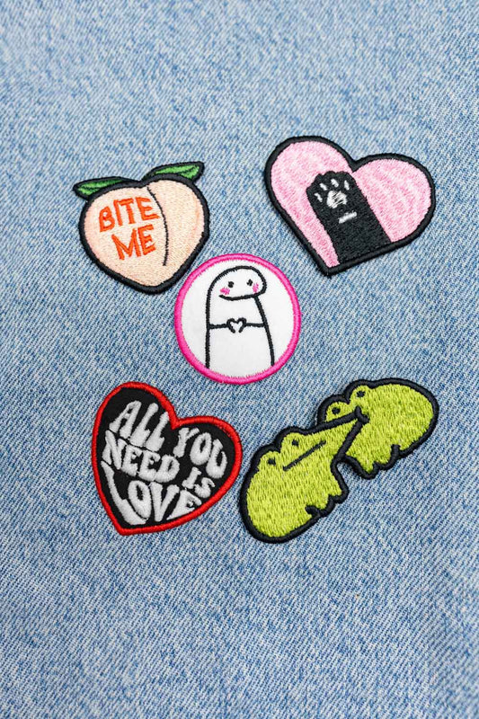 Set de cinci patch-uri brodate cu designuri drăguțe și colorate, incluzând piersică cu mesajul „Bite Me”, pisică, inimă cu mesaj „All You Need Is Love” și broască, prezentate pe material denim.