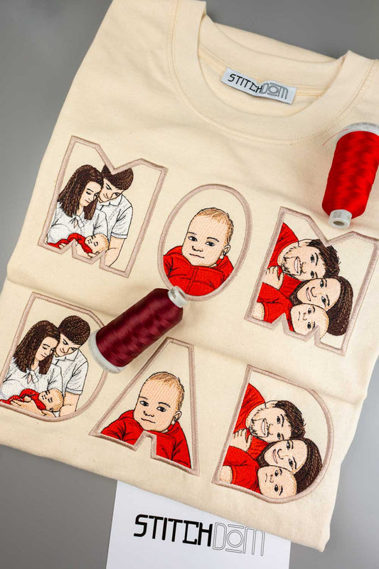 Set tricouri crem din bumbac organic, cu un design personalizat brodat care formează textul „MOM” si „DAD”, având portrete ilustrate de familie brodate în nuanțe de roșu și maro, alături de conuri de ață roșie și bordo așezate pe tricou, cu brandul „Stitchdom” vizibil pe eticheta de la gât și pe un card în partea de jos.