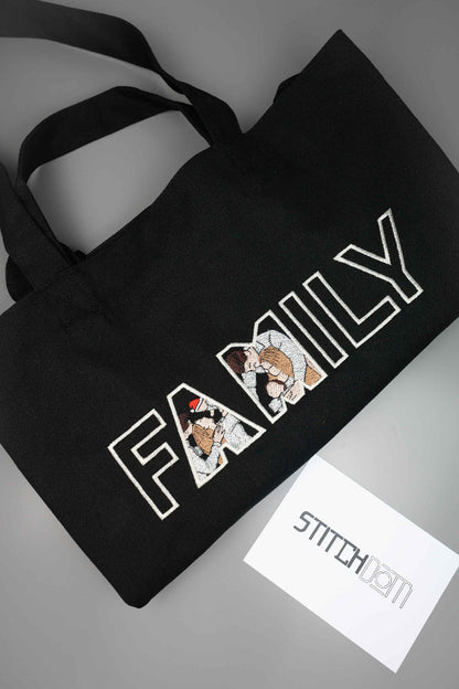 Geantă tote neagră din bumbac organic, pe un fundal gri, cu textul „FAMILY” și poze brodate cu personaje de familie, cu brandul „Stitchdom”.