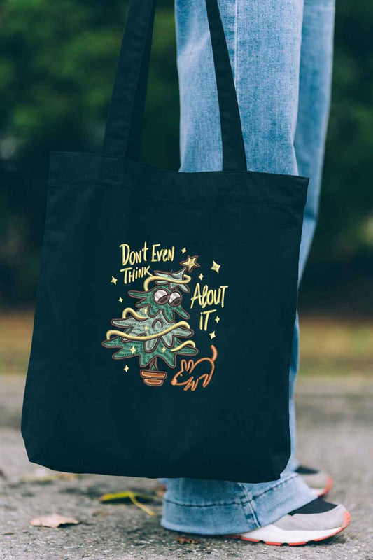 Tote bag brodat negru cu ilustrație amuzantă a unui copăcel în ghiveci și mesajul „Don't Even Think About It”, purtat în aer liber.