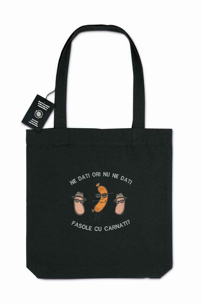 Tote bag brodat negru cu ilustrație amuzantă cu boabe de fasole purtând pălării și ochelari de soare și mesajul românesc „Ne dați ori nu ne dați fasole cu cârnați?”, purtat în aer liber.