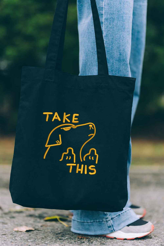 Tote bag brodat negru cu text galben „Take This” și ilustrație de câine, un design amuzant purtat în aer liber.